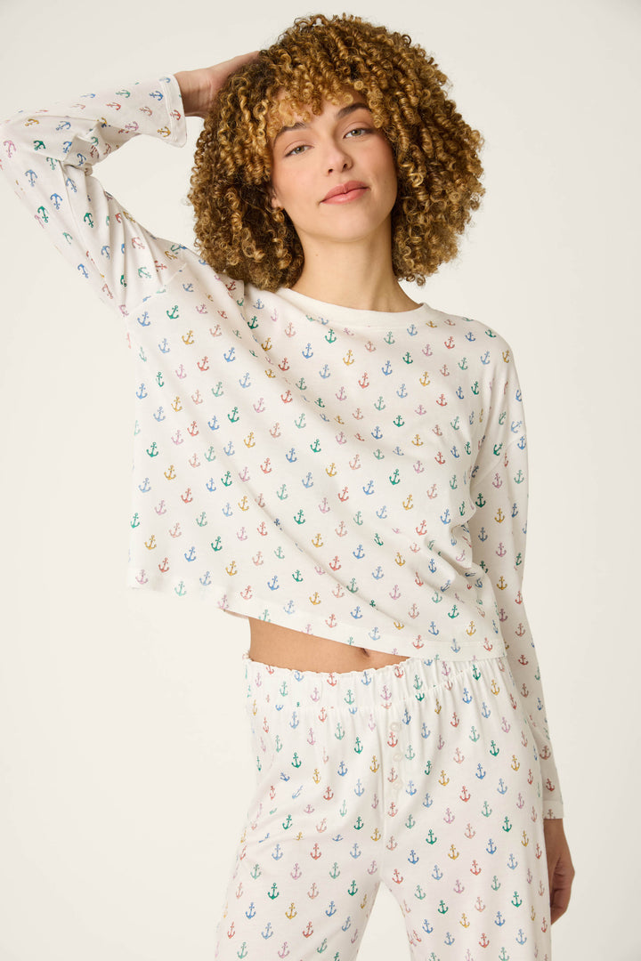 A person with curly hair wears a long-sleeve top featuring colorful anchor patterns, raising one arm against a plain background.