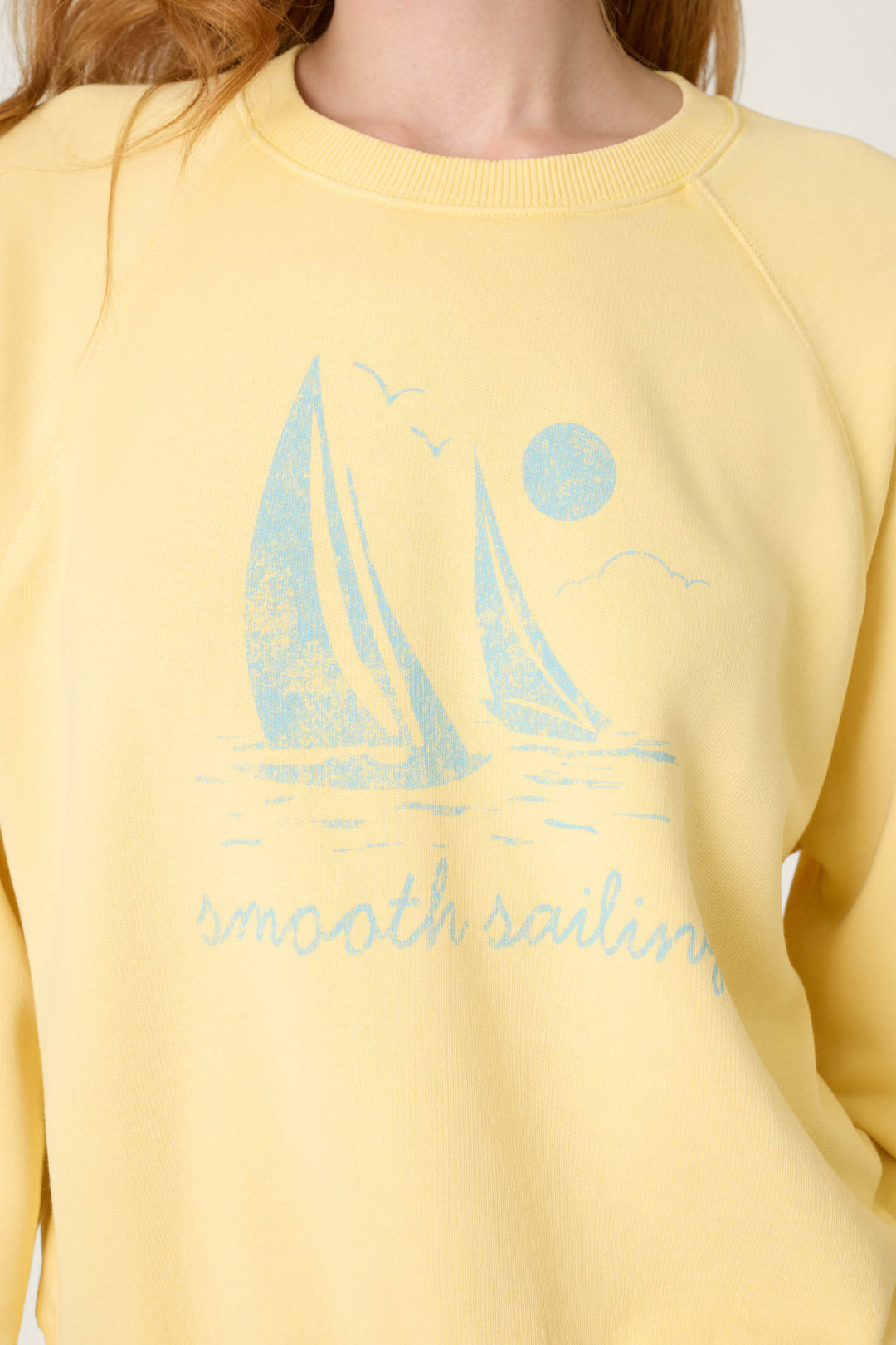 Light yellow fabric with a smooth texture, featuring a blue graphic of two sailboats, birds, the sun, and "smooth sailing.