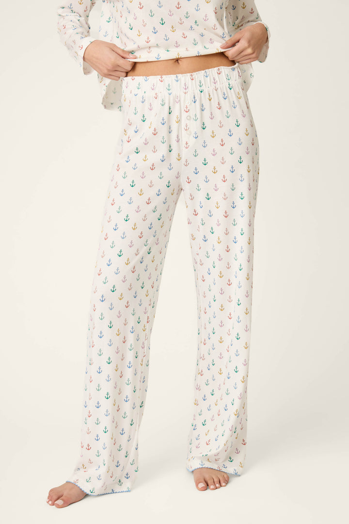 A person stands barefoot against a light background, wearing rainbow anchor print pajama pants; focus is on the pants and waist.