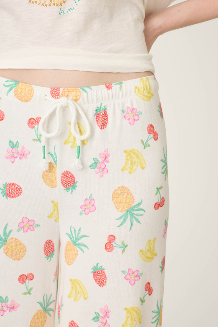 White fabric with a colorful print of pineapples, bananas, cherries, strawberries, and pink flowers.