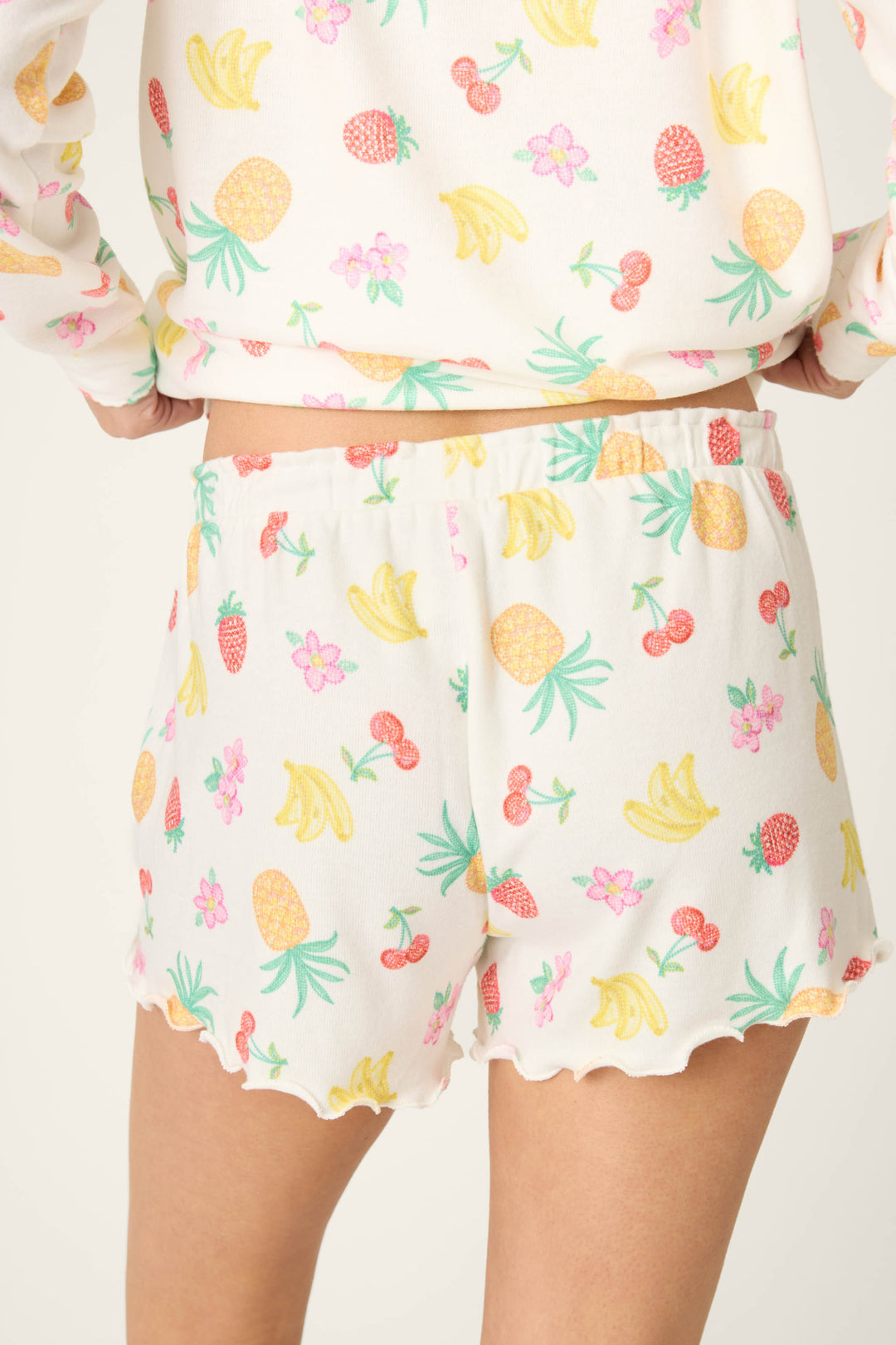 White fabric with a vivid fruit print featuring bananas, pineapples, strawberries, and cherries on a smooth surface.