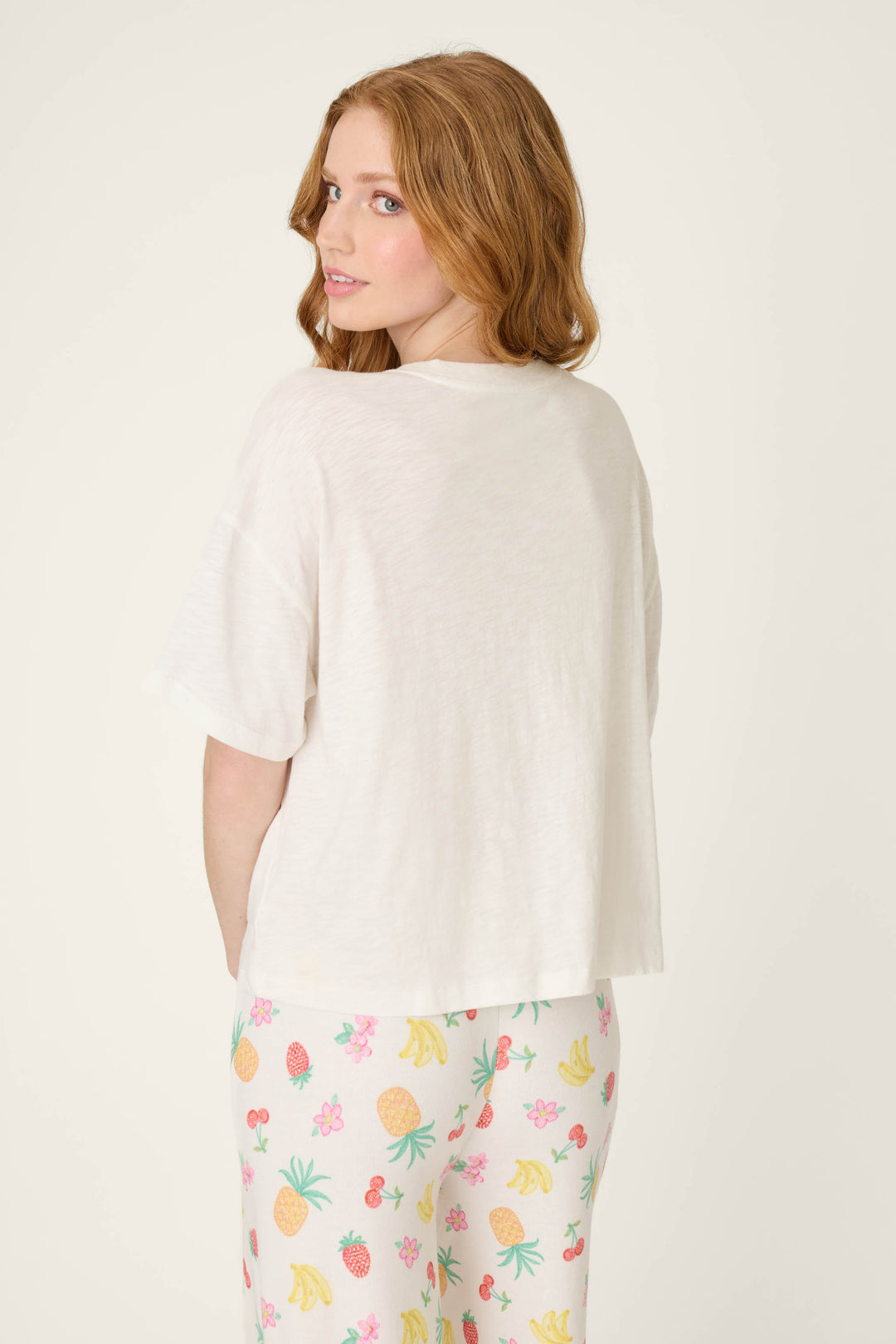 White fabric with vibrant multi-colored fruit patterns; smooth surface and playful, summery design.