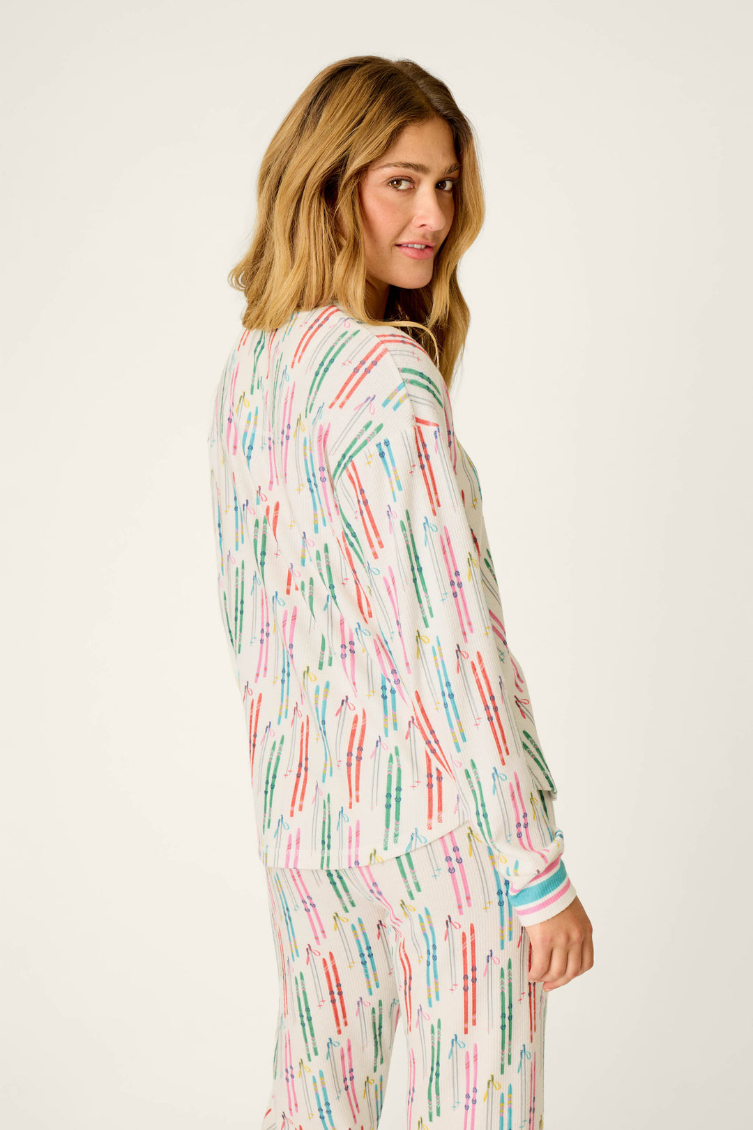A person with wavy, light brown hair wears the P.J. Salvage Après All Day Ski Print Long Sleeve Henley Top, looking over their shoulder and smiling softly against a plain light background.