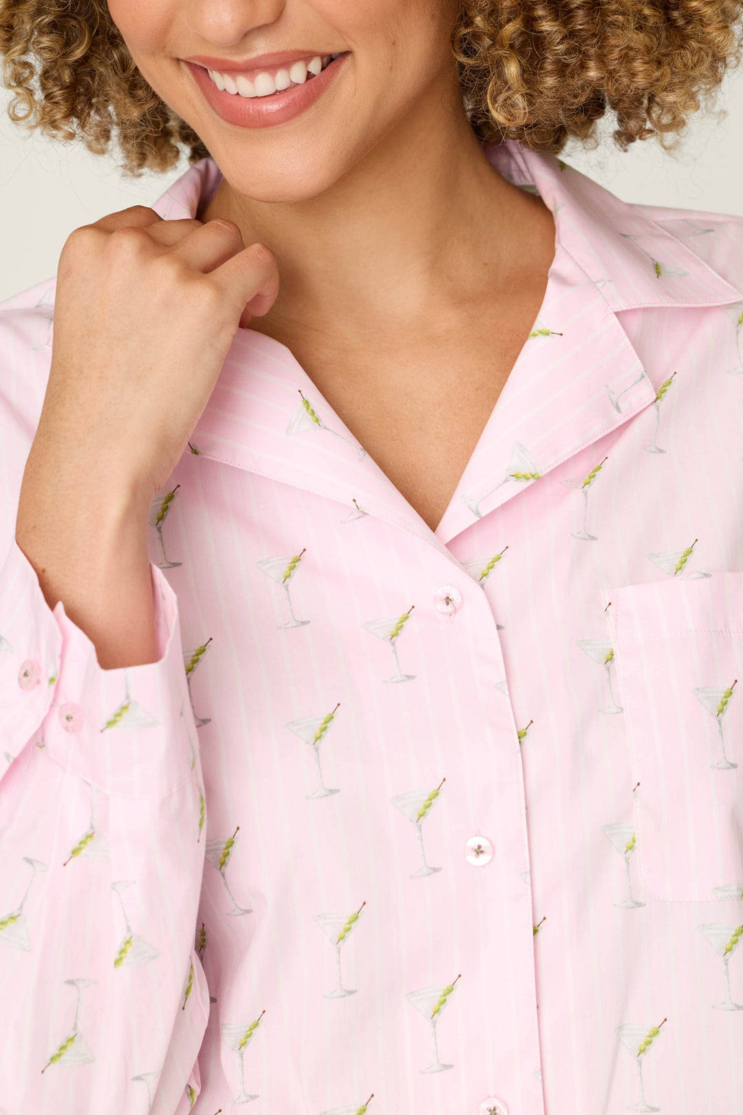 A smiling person, visible from the lower face to upper torso, lightly touches the collar of the P.J. Salvage Afterparty Poplin Stripe & Martini Print Long Sleeve Top.