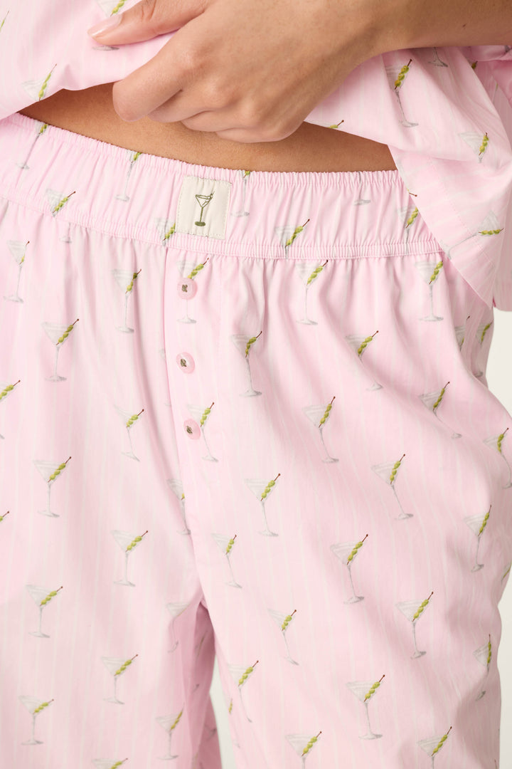 A person wears the Afterparty Poplin Stripe & Martini Print Pajama Pants by P.J. Salvage, featuring a light pink martini glass print, buttons, and an elastic waistband, with their hand resting near the waist.