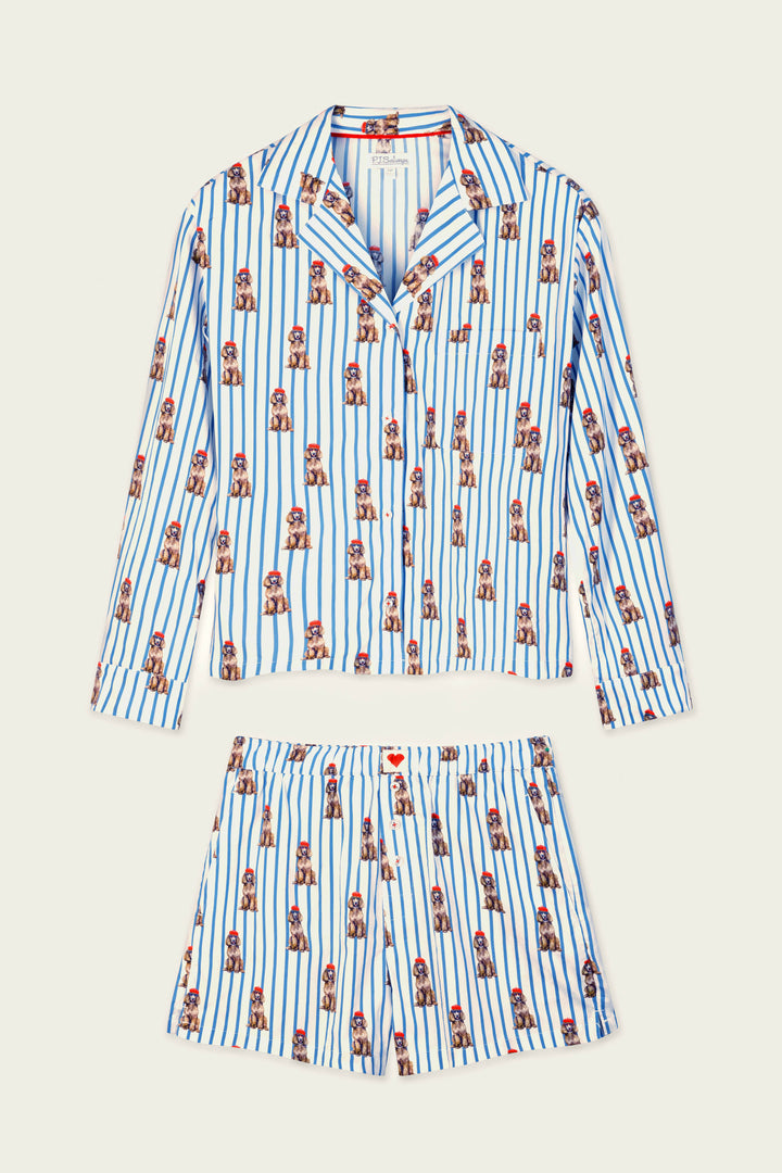 The P.J. Salvage Afterparty Poplin Stripe & Poodle Print Long Sleeve & Shorts PJ Set is a two-piece pajama set featuring a button-up long-sleeve top and shorts, crafted from white fabric with vertical blue stripes and adorned with a repeating print of small brown poodles wearing red hats.