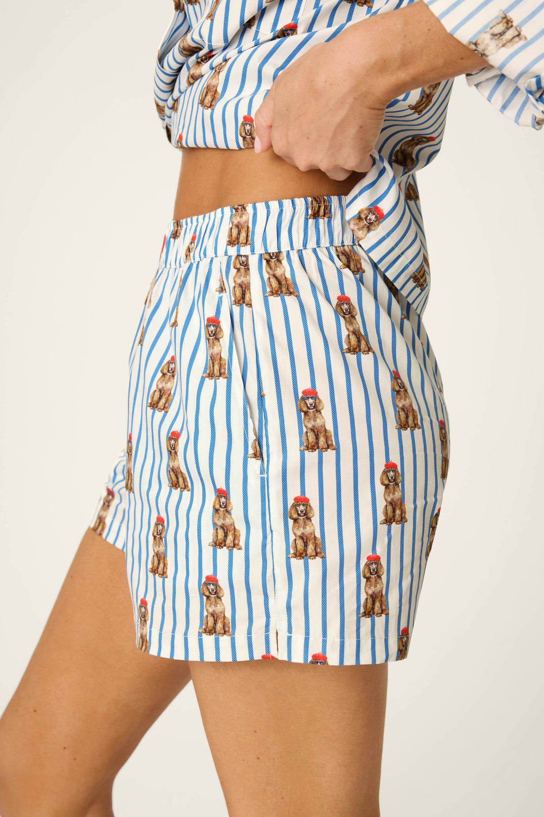 Model wears the P.J. Salvage Afterparty Poplin Stripe & Poodle Print Pajama Shorts, shown from mid-torso to mid-thigh, with one hand adjusting the waistband.