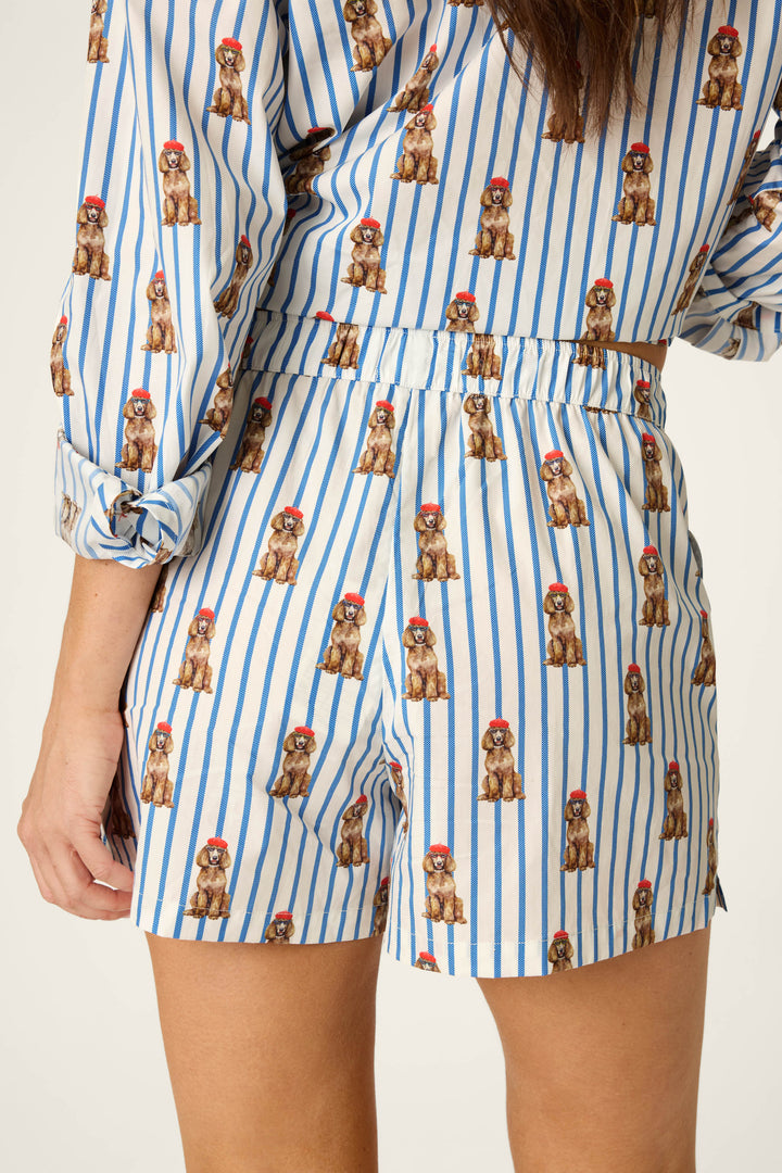 A person models the P.J. Salvage Afterparty Poplin Stripe & Poodle Print Pajama Shorts, featuring blue and white stripes with a poodle print, shown from the back view, waist to mid-thigh.