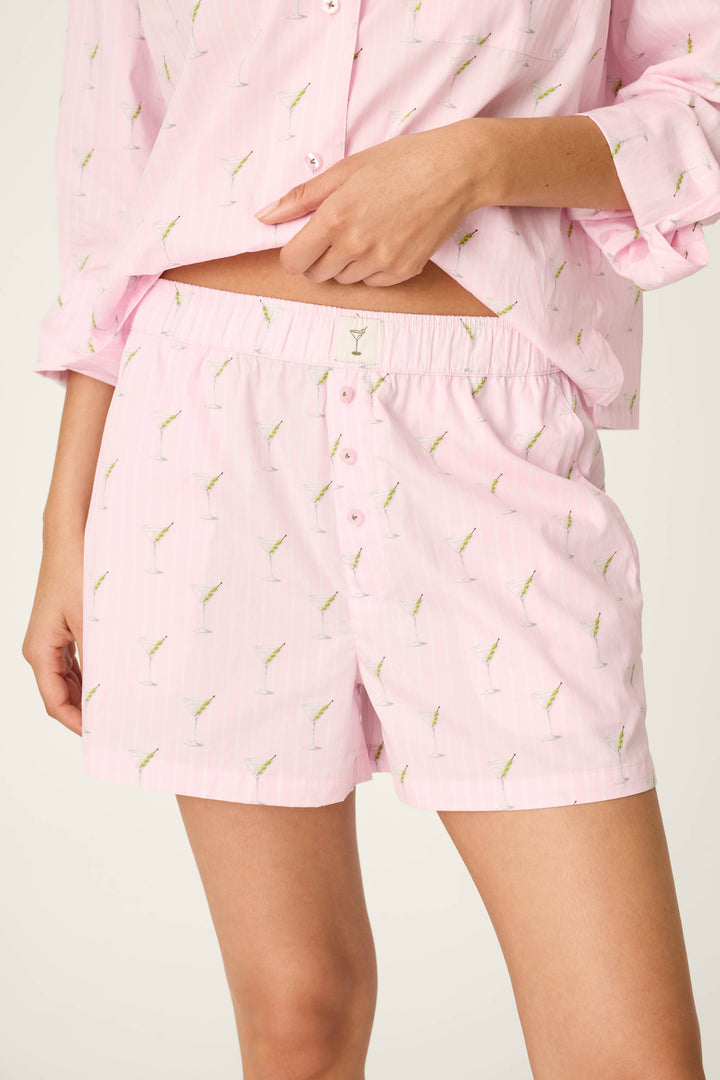 Wearing the P.J. Salvage Afterparty Poplin Stripe & Martini Print Pajama Shorts and a matching top, the person is dressed in light pink sleepwear featuring a small cocktail glass pattern. The image displays the outfit from mid-thigh to mid-torso.