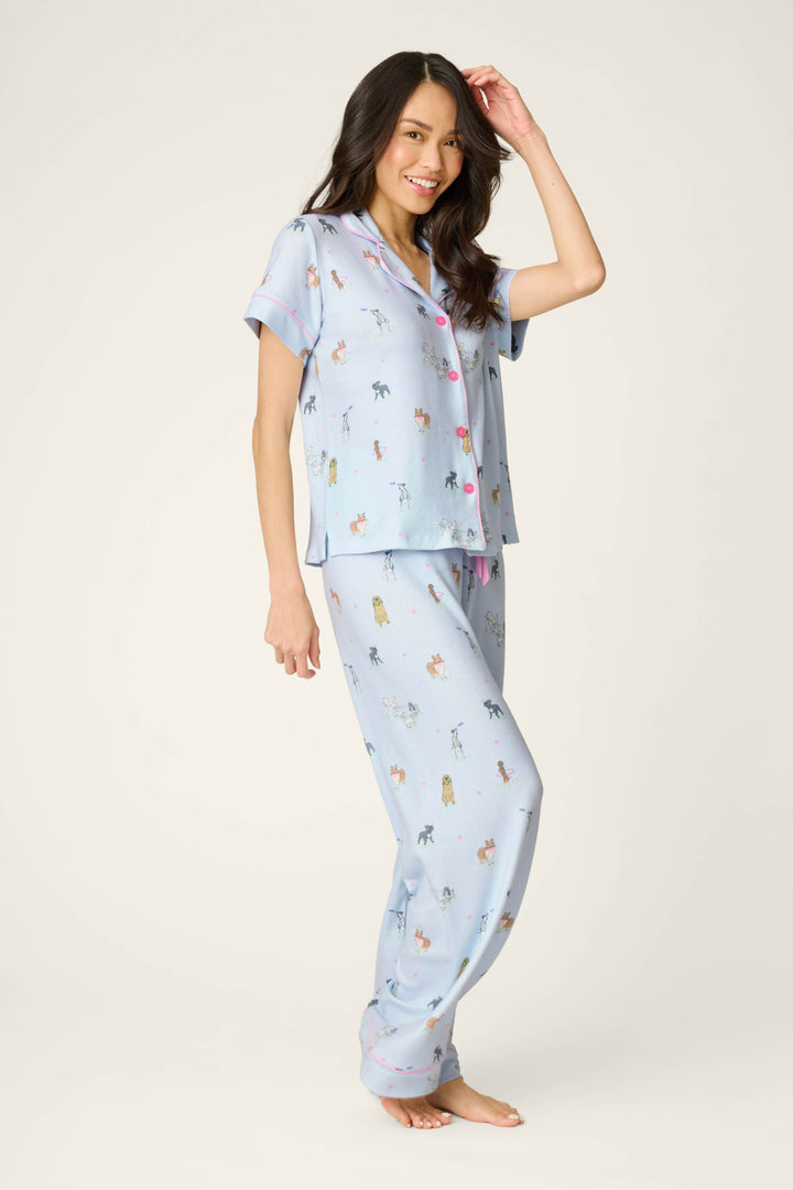 A woman with long dark hair smiles barefoot in the P.J. Salvage Bark Park Fetch & Frolic 3-Piece PJ Set, featuring a playful dog print, perfect for women’s sleepwear, posed against a plain light background.