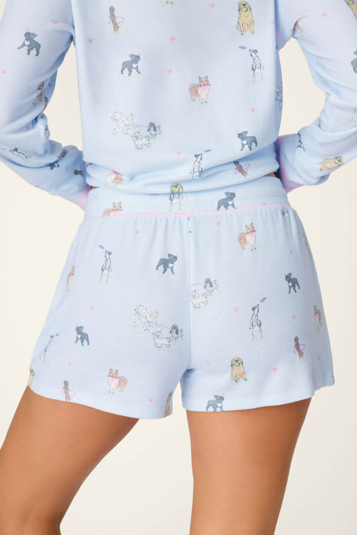 Someone wearing the Bark Park Fetch & Frolic Sleep Shorts by P.J. Salvage, a light blue sleepwear set with playful dog prints, stands with hands on hips, facing away from the camera.