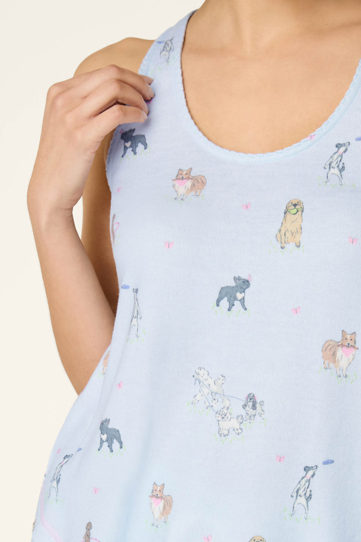 A person wears the P.J. Salvage Bark Park Fetch & Frolic Tank Top, a light blue women's loungewear sleep tank featuring a playful dog print. Their hand gently touches the strap near their shoulder.