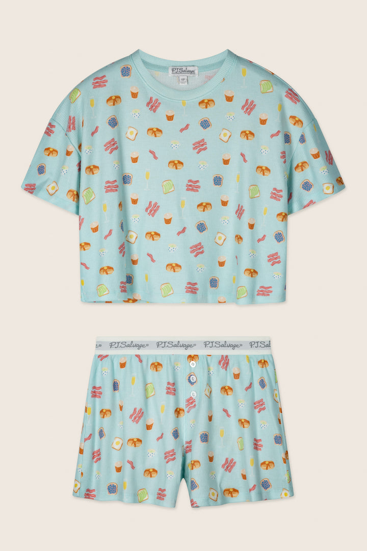 The Boyfriend Boxer Sunday Brunch Short PJ Set by P.J. Salvage features a light blue short-sleeve cropped top and matching shorts with a fun breakfast print of eggs, bacon, toast, and coffee, plus a branded waistband.