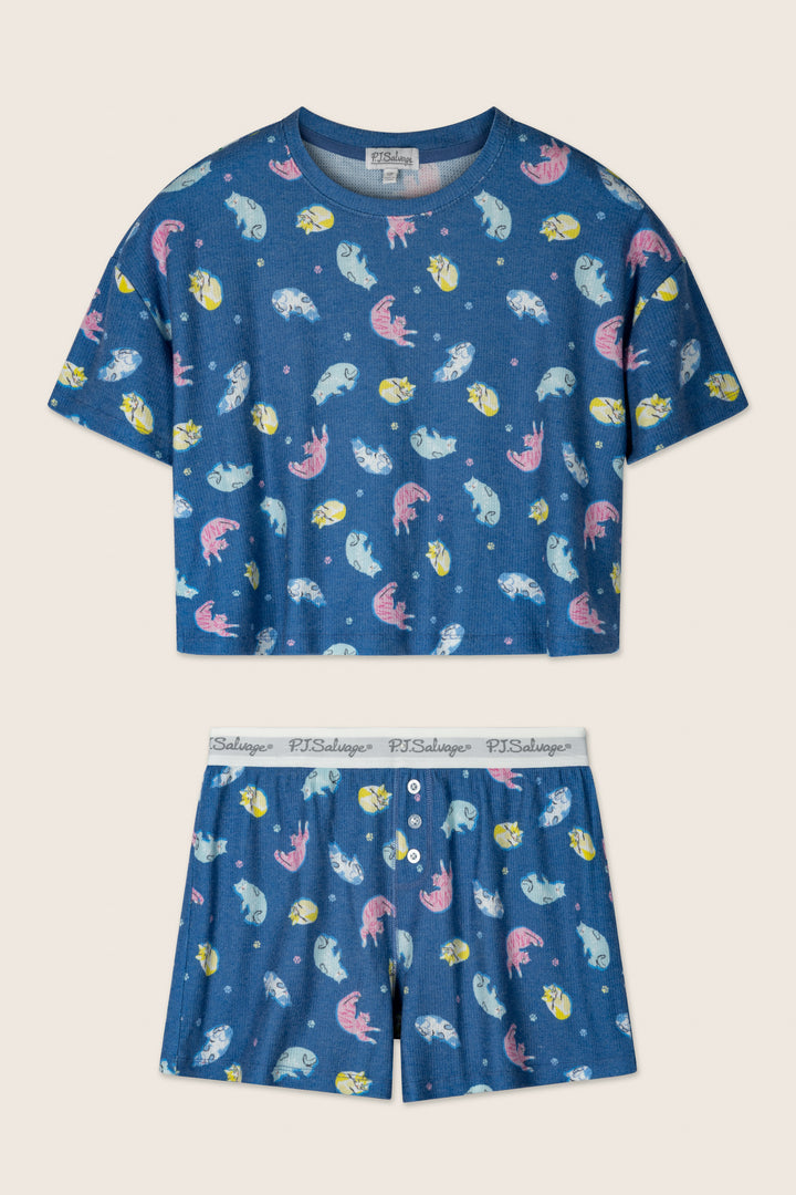 The Boyfriend Boxer Cat Nap Short PJ Set by P.J. Salvage is a blue short-sleeve pajama set with matching shorts, featuring colorful fish and a white elastic waistband with “P.J. Salvage” branding.
