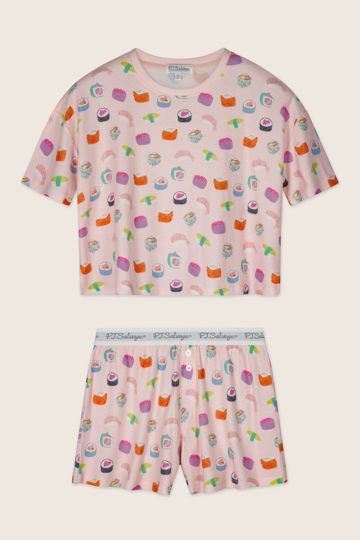 The Boyfriend Boxer Sushi Bites Short PJ Set by P.J. Salvage features a pink short-sleeve top and shorts with a colorful sushi print and a white elastic waistband displaying "PJ Salvage" in gray text.