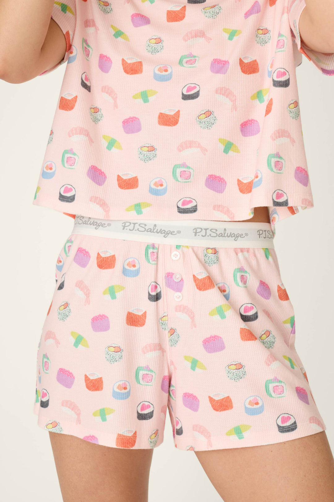Person models the Boyfriend Boxer Sushi Bites Short PJ Set by P.J. Salvage—matching pink pajamas with colorful sushi prints and white waistband branded "P.J. Salvage." The person’s face is not shown.