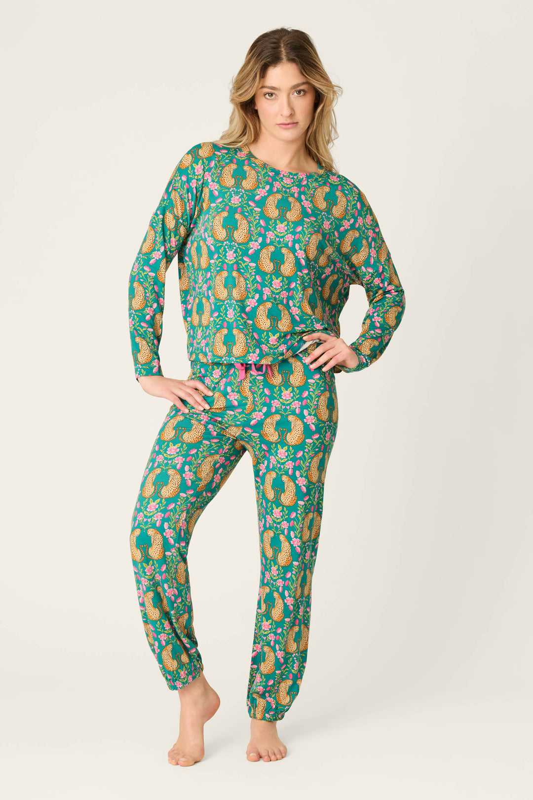 A person stands barefoot wearing the P.J. Salvage Cheetah Bonita Dreams Cheetah Print Long Sleeve Top. They pose with one hand on their hip and the other relaxed, facing forward against a plain light background.