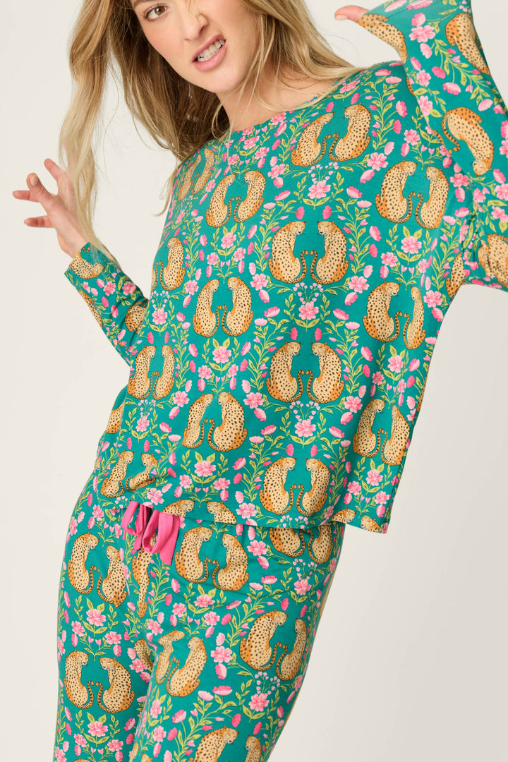 A woman models the P.J. Salvage Cheetah Bonita Dreams Cheetah Print Long Sleeve Top, featuring a vibrant teal hue with playful cheetah and pink floral motifs, striking a fun pose against a light background.