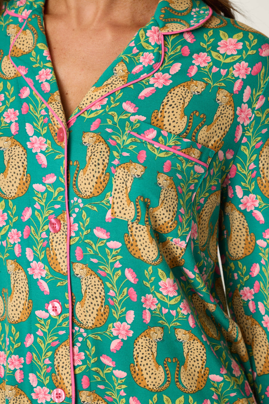 Close-up of a person wearing the P.J. Salvage Cheetah Bonita Dreams Cheetah Print Long Sleeve PJ Set, featuring a teal pajama top adorned with a colorful pattern of cheetahs, pink flowers, and green leaves. The top includes a chest pocket and pink buttons.