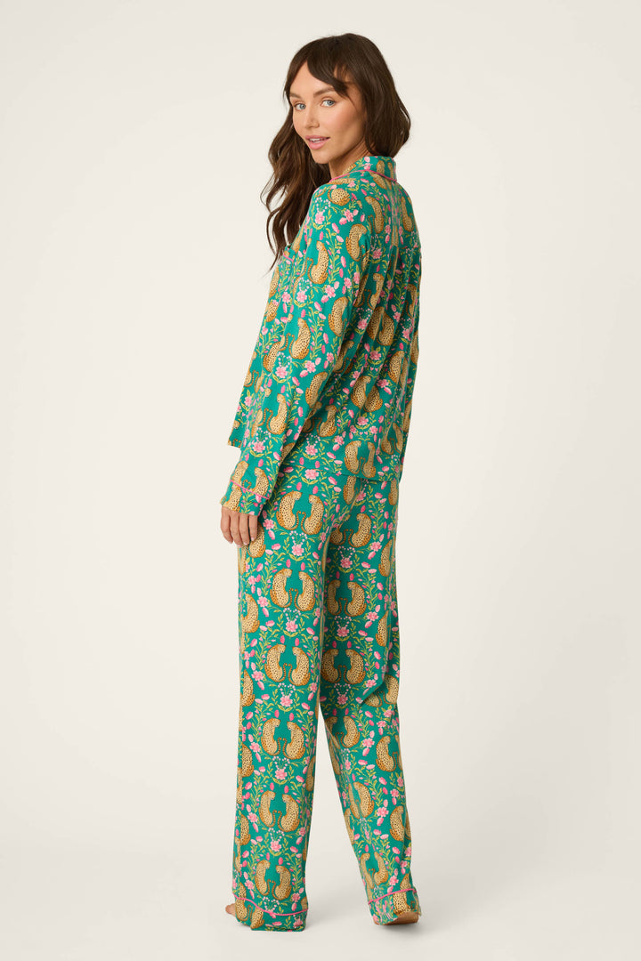 A woman stands barefoot, turned to the side, wearing the P.J. Salvage Cheetah Bonita Dreams Cheetah Print Long Sleeve PJ Set. She has long brown hair and looks over her left shoulder at the camera against a neutral background.