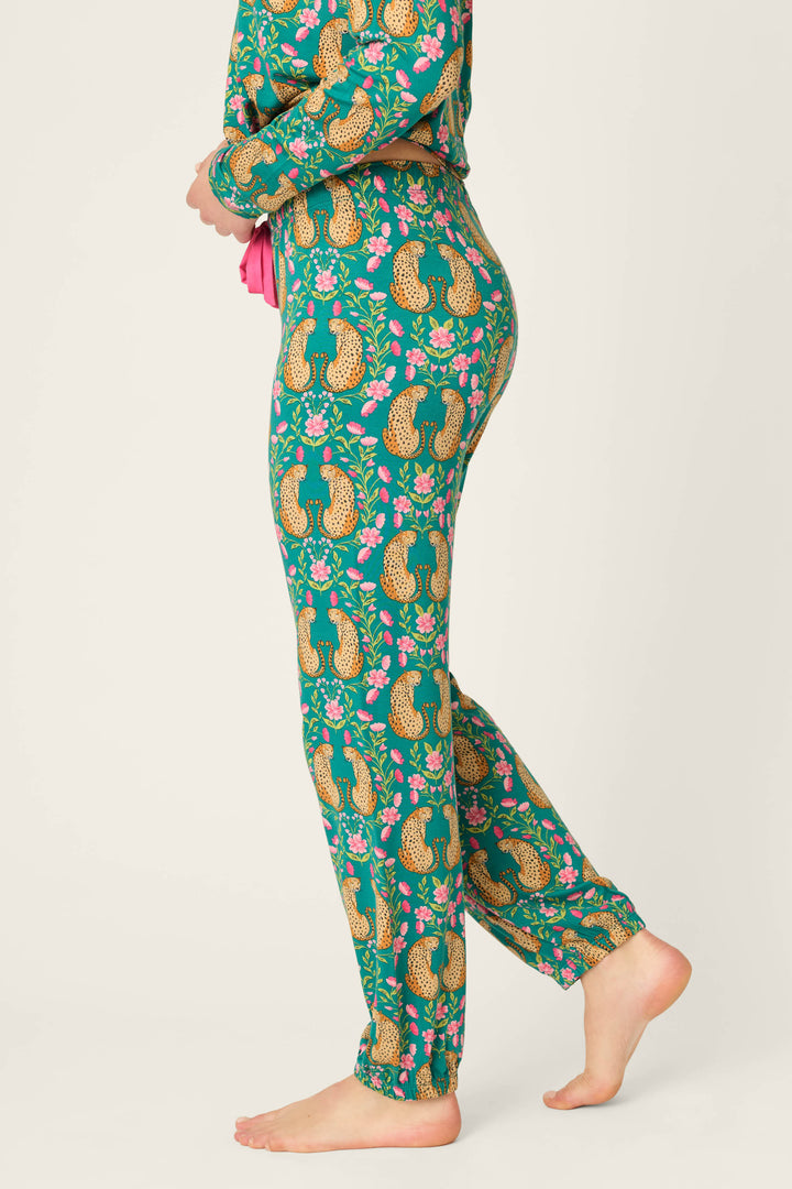 A person stands barefoot in P.J. Salvage's Cheetah Bonita Dreams Cheetah Print Pajama Joggers, featuring a vibrant leopard and floral pattern, shown from the side against a plain background.