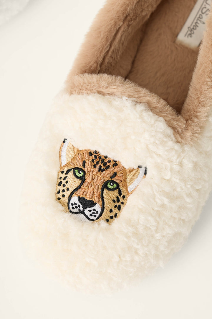 A close-up of a fluffy cream slipper with an embroidered cheetah face on the toe area. The slipper has a soft tan interior lining and a fuzzy cream exterior.