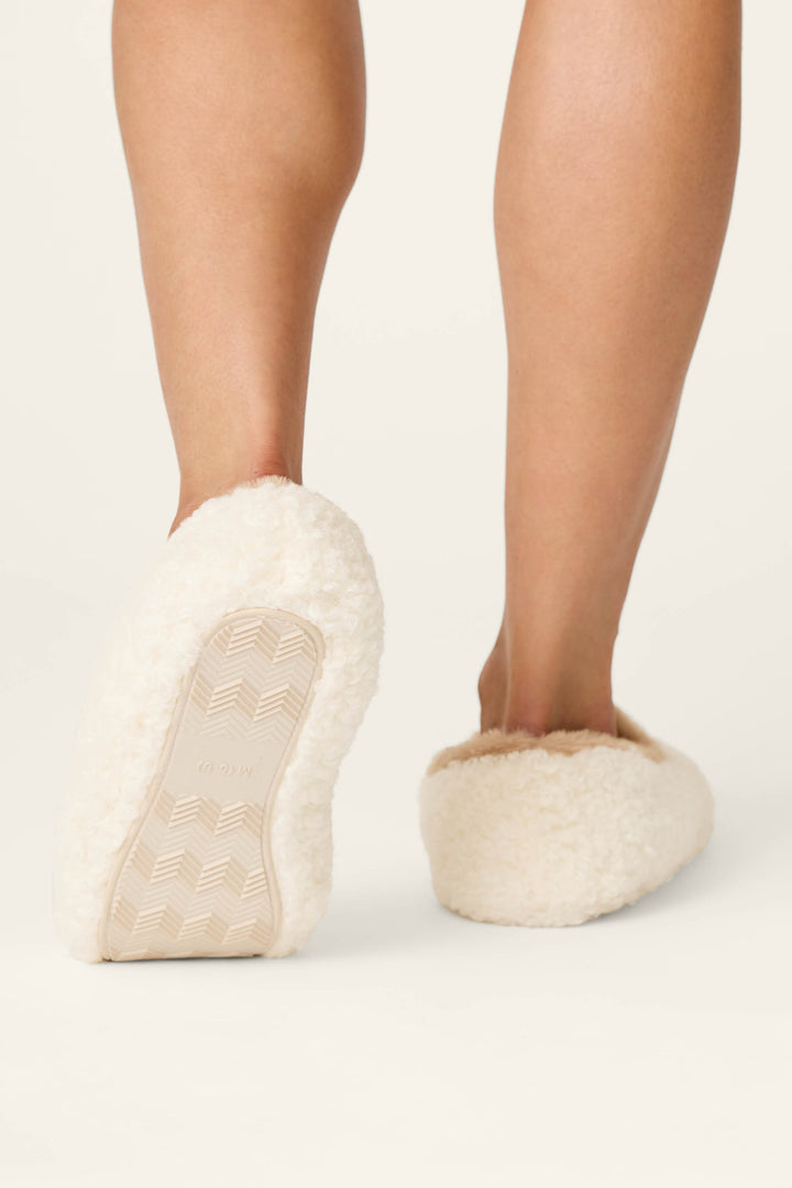 A person is shown from behind, with only their lower legs and feet visible, wearing P.J. Salvage Cheetah Bonita Dreams Embroidered Cheetah Slippers as they walk away on a light background.