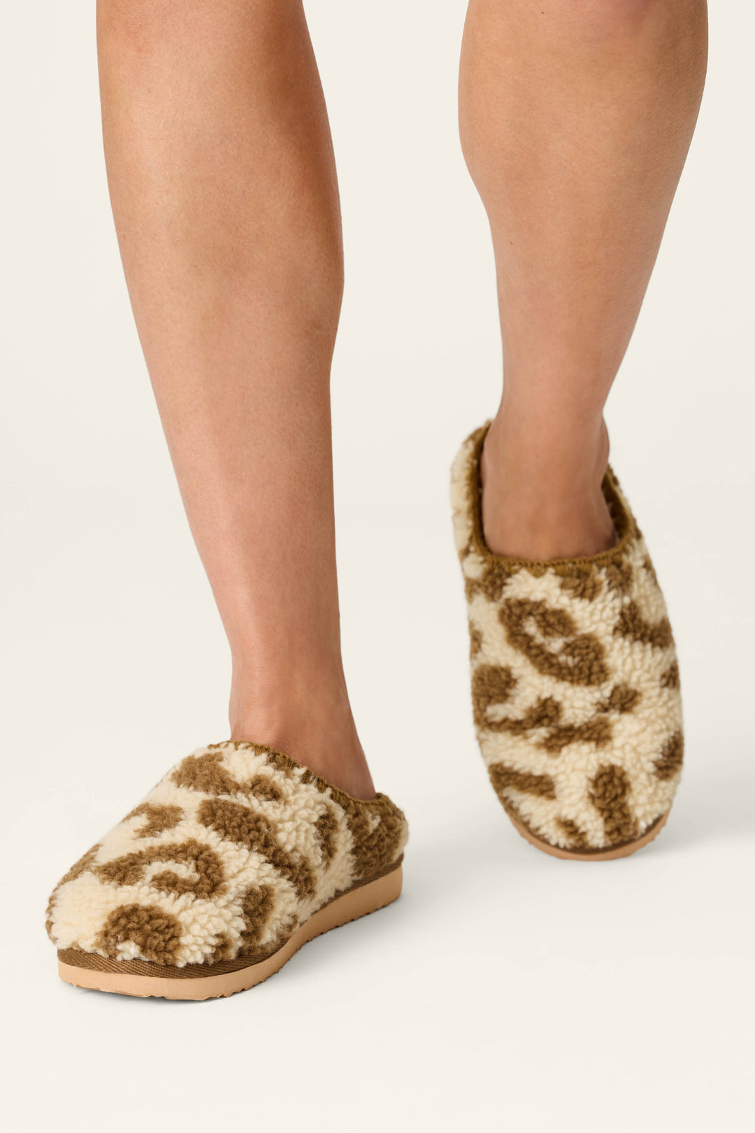 A person wearing P.J. Salvage Cheetah Bonita Dreams cheetah print fuzzy slippers is standing on a light-colored surface.