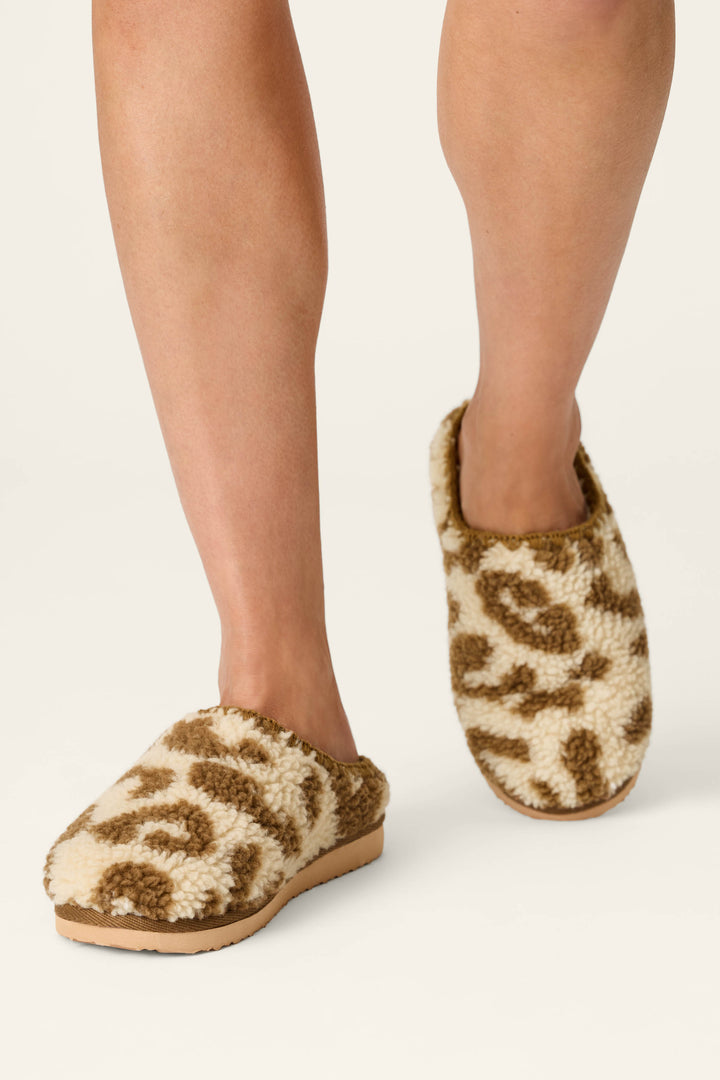 A person wearing P.J. Salvage Cheetah Bonita Dreams cheetah print fuzzy slippers is standing on a light-colored surface.