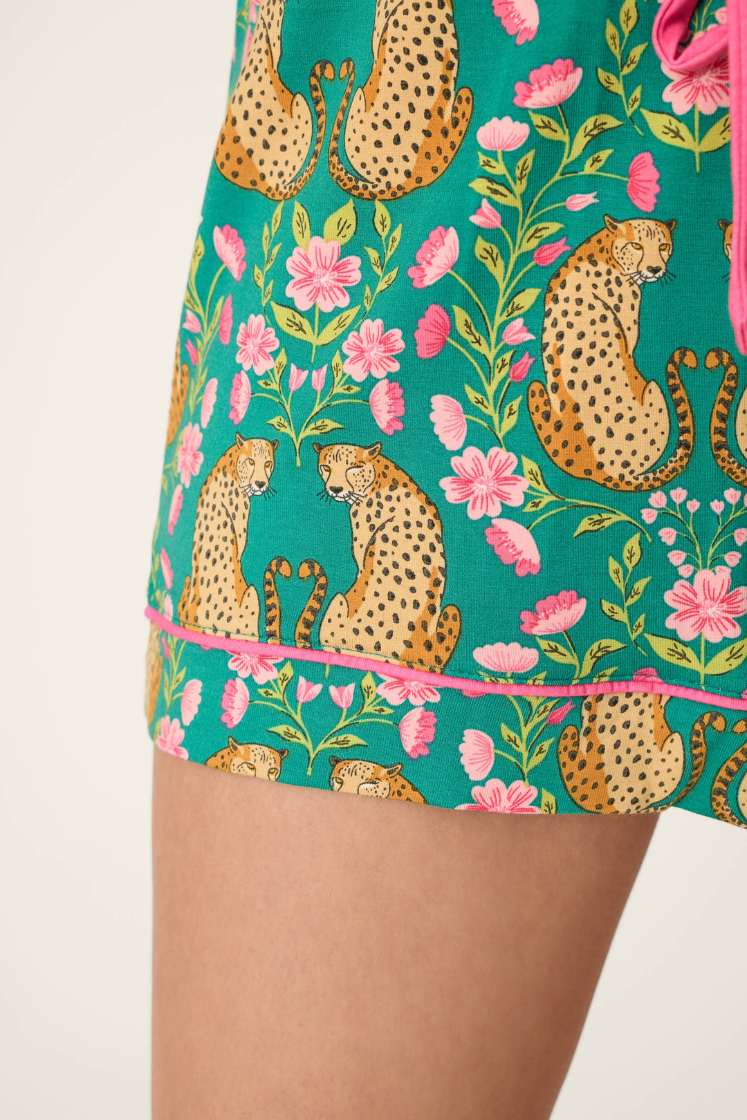 Close-up of a person's leg wearing P.J. Salvage Cheetah Bonita Dreams Cheetah Print Pajama Shorts, featuring green fabric with cheetahs and pink flowers.