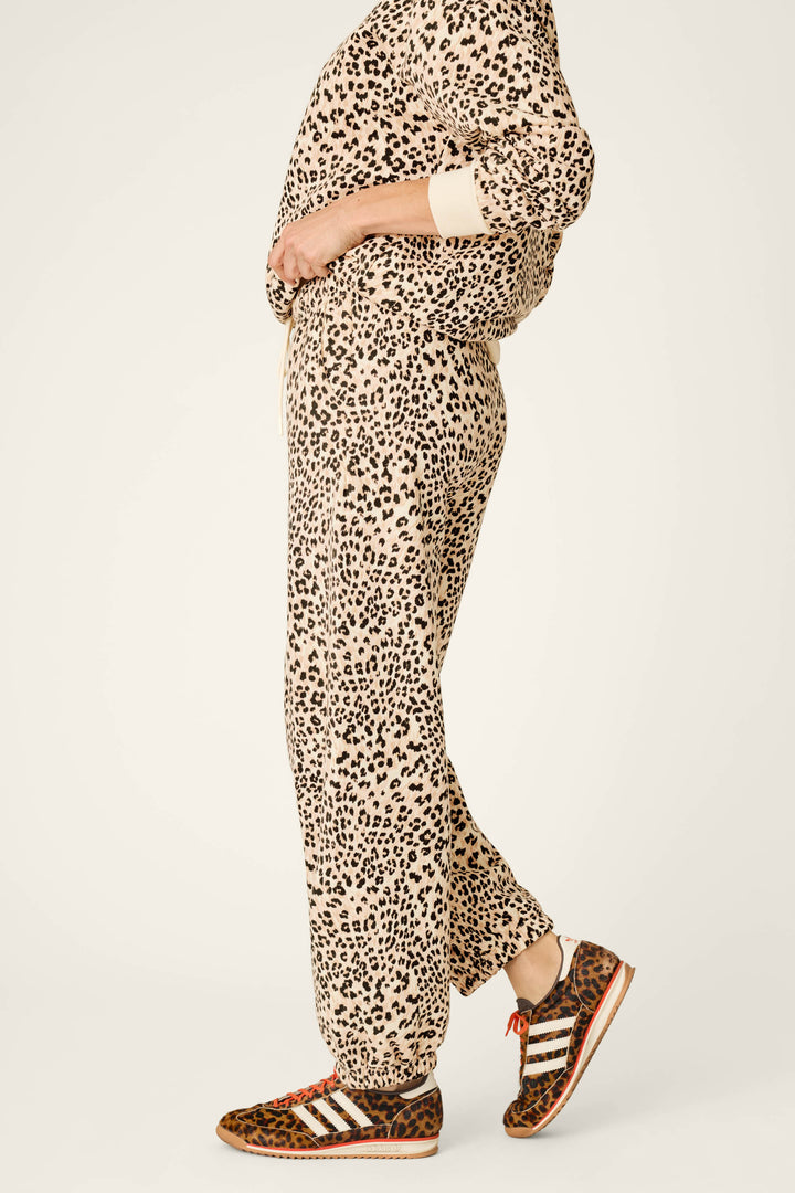 A person models the P.J. Salvage C'est La Vie Leopard Print Good Hang Jogger Pants, standing with hands in pockets and facing sideways against a plain light background.