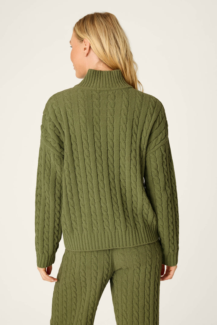 A person with long blonde hair is seen from the back against a plain light background, wearing the P.J. Salvage Cozy Chenille Cable Knit Olivine Pullover sweater paired with matching pants.