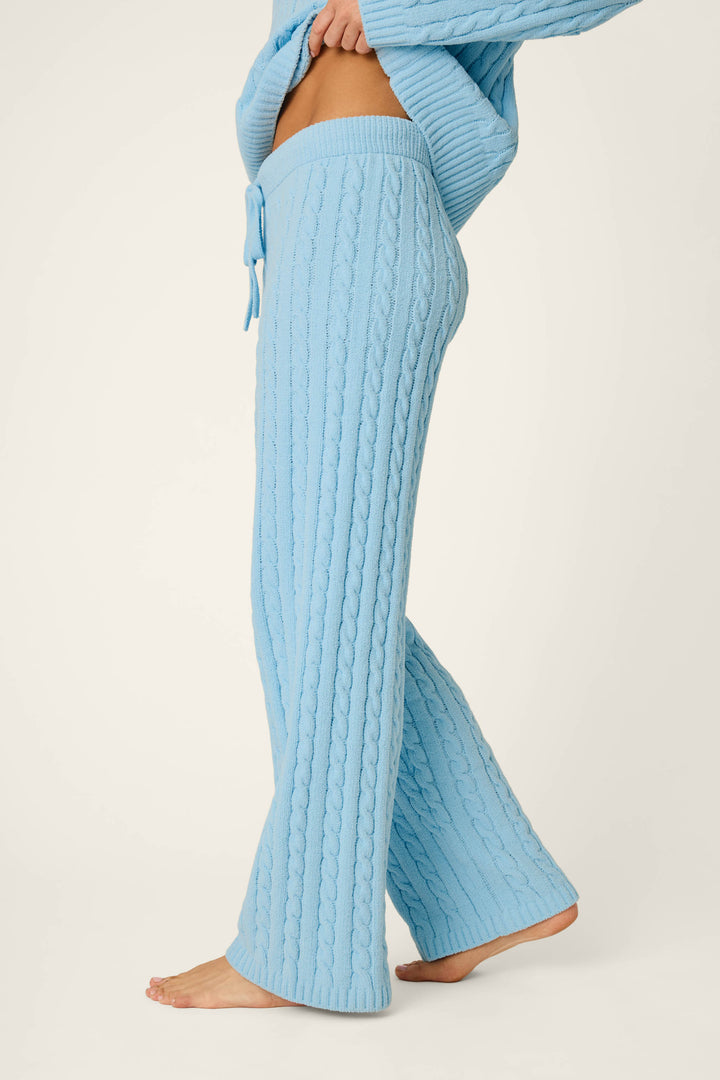 A person—barefoot and shown only from the waist down—wears P.J. Salvage’s Cozy Chenille Cable Knit Cloud Blue Lounge Pants, styled with a matching sweater, against a plain background.