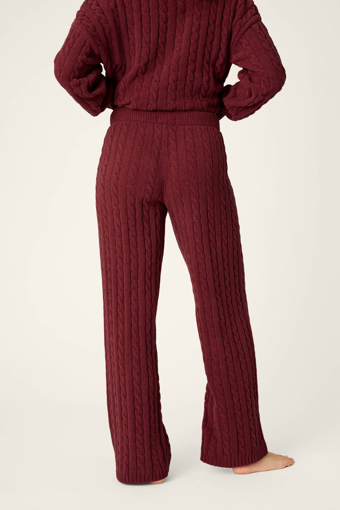 A person stands barefoot, facing away, wearing P.J. Salvage Cozy Chenille Cable Knit Dark Wine Lounge Pants against a plain light background.
