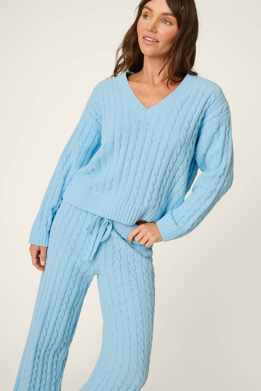 A woman wearing the P.J. Salvage Cozy Chenille Cable Knit Cloud Blue V-Neck Lounge Set poses with one hand on her hip. The set features a relaxed fit, creating a cozy and casual look.