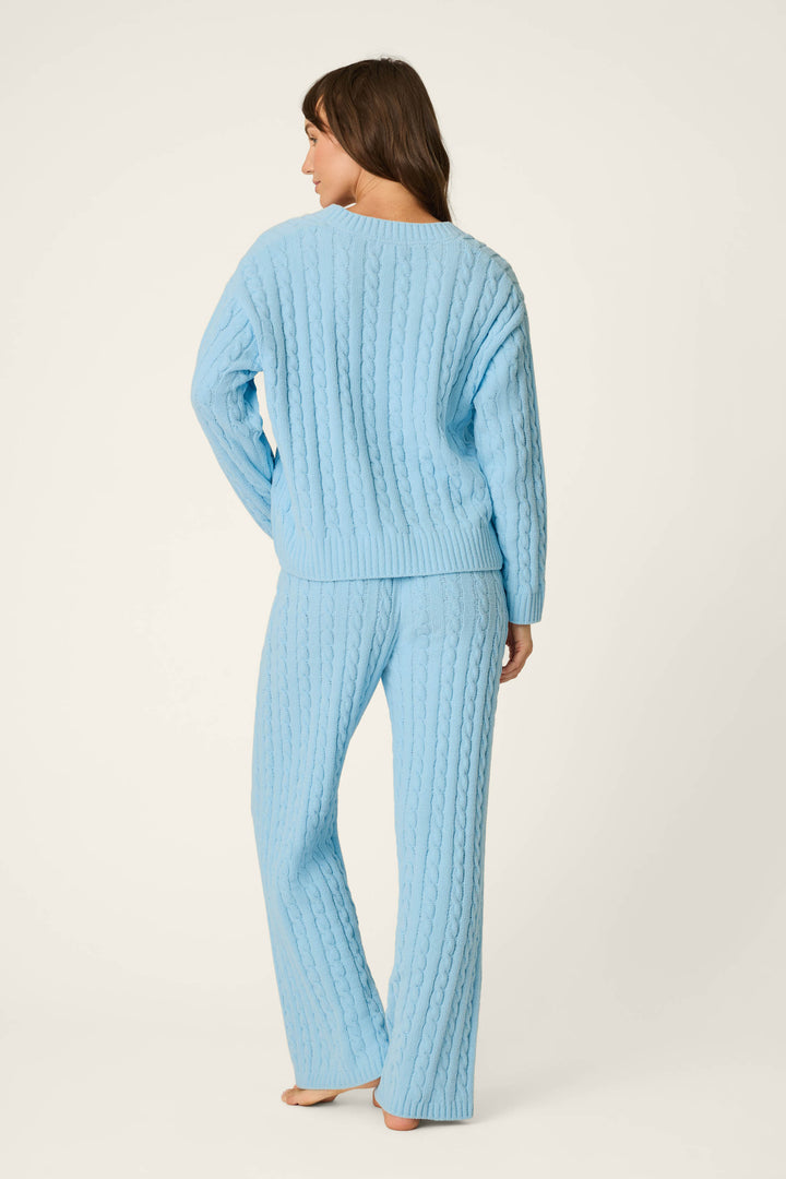 A woman stands barefoot facing away, wearing the P.J. Salvage Cozy Chenille Cable Knit Cloud Blue V-Neck Lounge Set. Her brown hair rests on her shoulders against a plain white background.