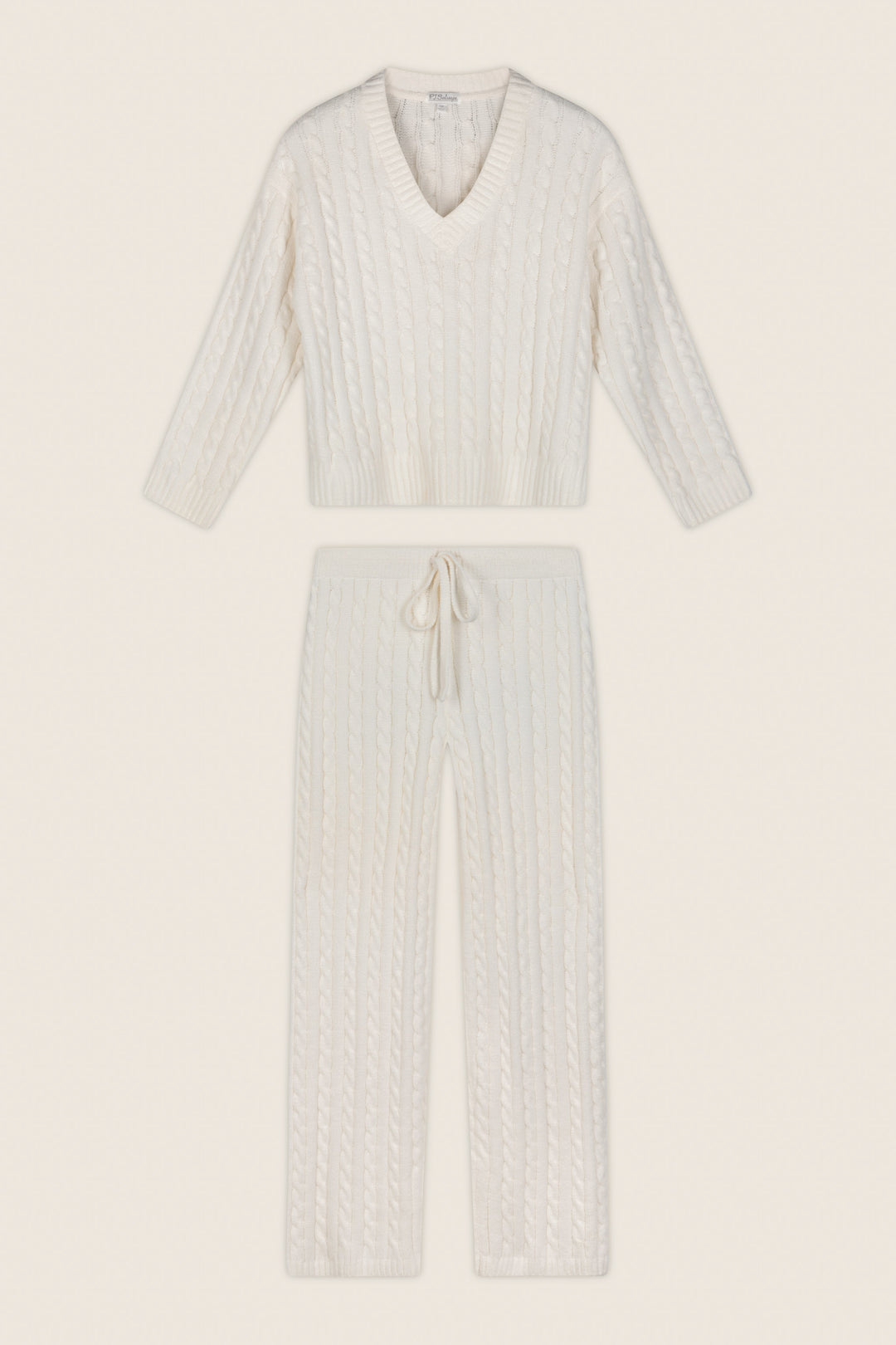 A two-piece knit loungewear set in an off-white/cream color, featuring a long-sleeve V-neck sweater and matching drawstring pants, laid flat against a solid cream background.