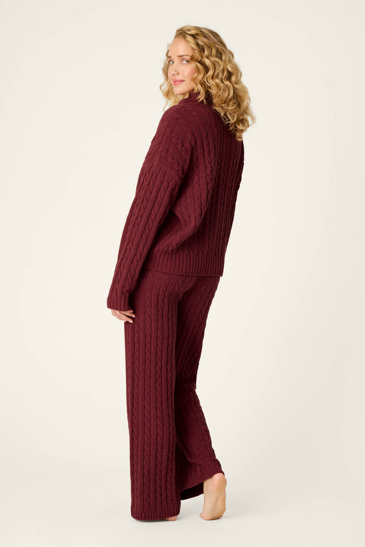 A woman with curly blonde hair stands barefoot against a plain light background, looking over her shoulder while wearing the P.J. Salvage Cozy Chenille Cable Knit Dark Wine Pullover Lounge Set.