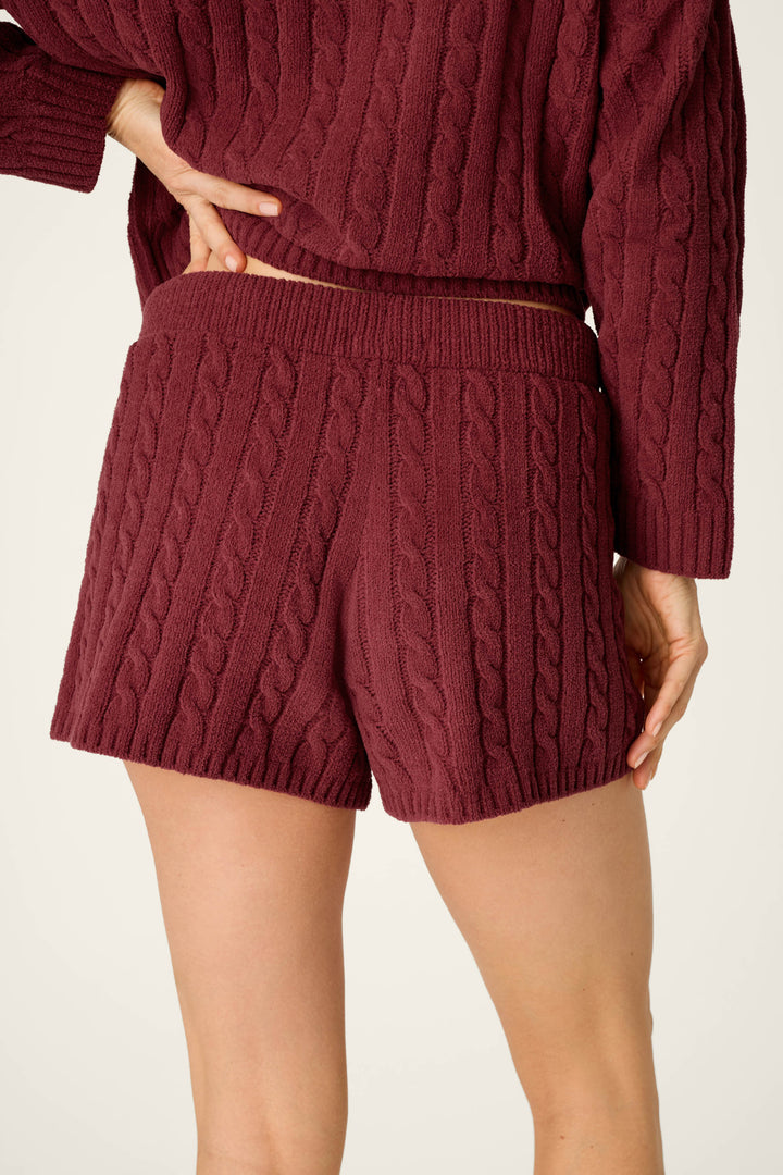 Model wearing P.J. Salvage Cozy Chenille Cable Knit Dark Wine Lounge Shorts, paired with a matching sweater, shown from the back with one hand on their hip against a plain light background.