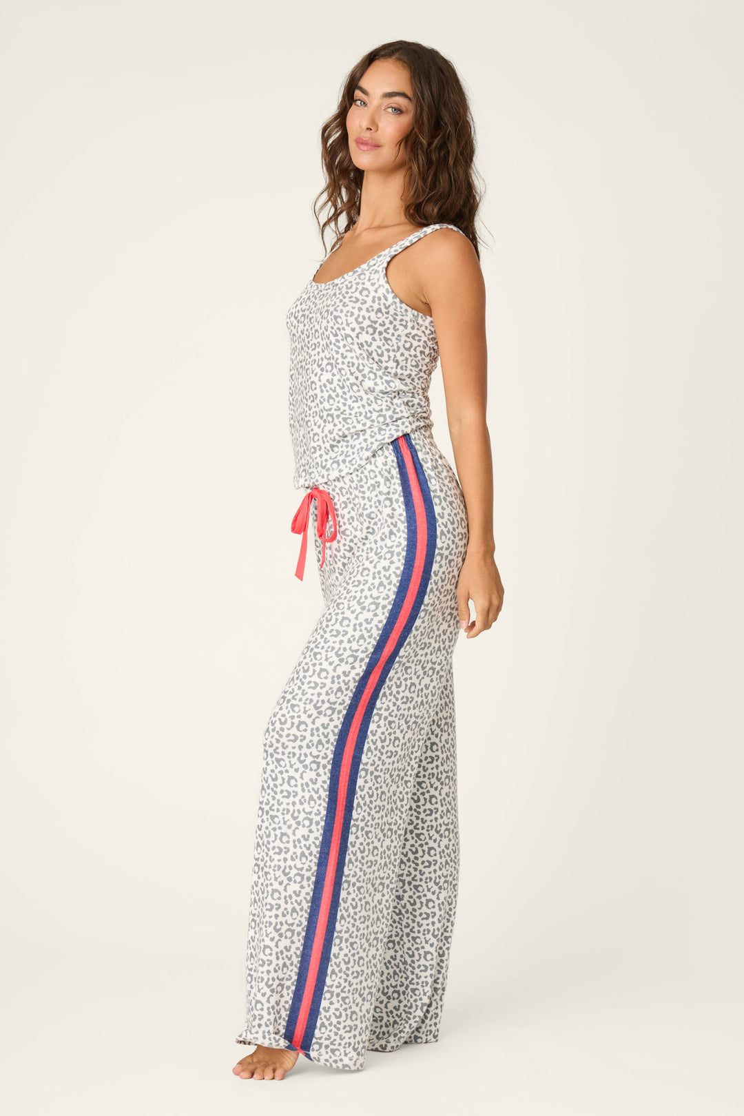 A woman wearing the P.J. Salvage Cat’s Meow Big Stretch Long PJ Set—sleeveless leopard print top and wide-leg pajama pants with red and blue side stripes and a red drawstring—stands barefoot against a light background.