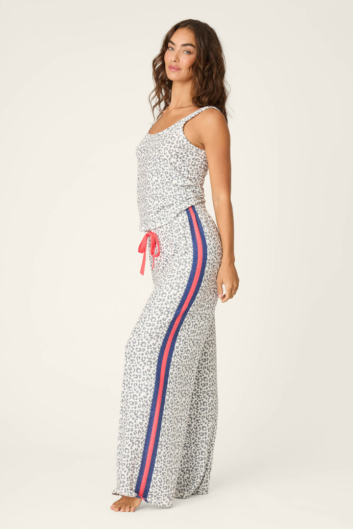 A woman wearing the P.J. Salvage Cat’s Meow Big Stretch Long PJ Set—sleeveless leopard print top and wide-leg pajama pants with red and blue side stripes and a red drawstring—stands barefoot against a light background.