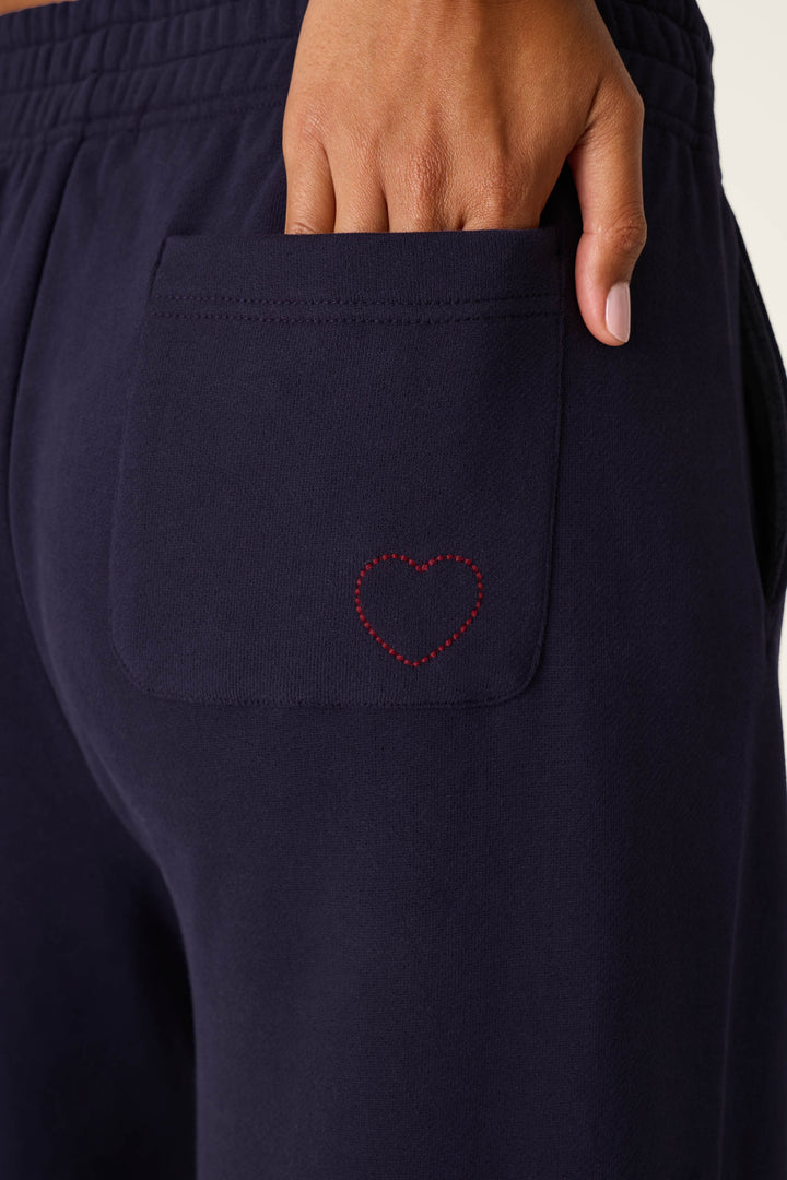 A hand rests in the back pocket of the P.J. Salvage C'est La Vie Blue Ink BFF Lounge Pants, which feature a small red stitched heart on the pocket.