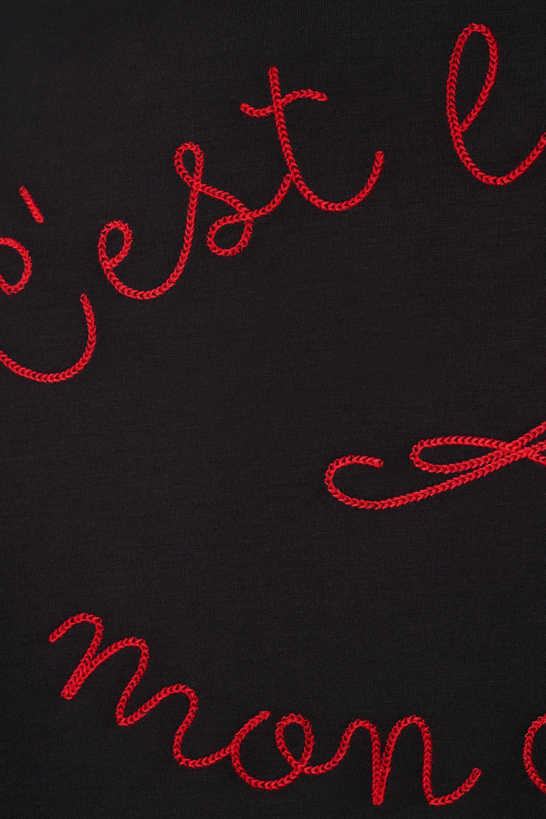 Close-up of a black fabric surface with red cursive embroidered lettering partially visible.