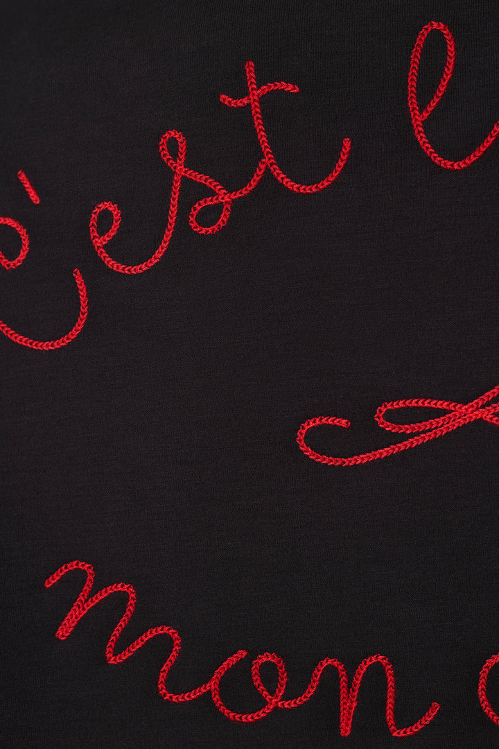 Close-up of a black fabric surface with red cursive embroidered lettering partially visible.