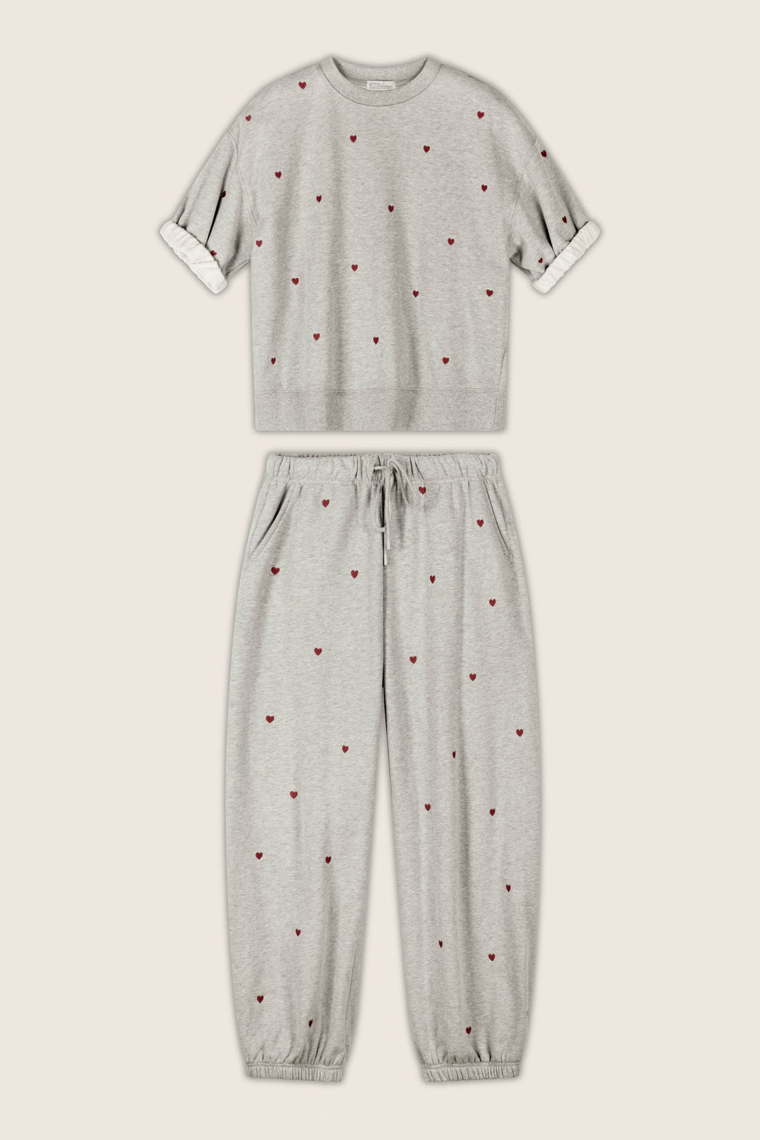 The P.J. Salvage C'est La Vie Embroidered Hearts Roll Back Short Sleeve Sweatshirt and coordinating jogger pants set, featuring small red heart embroidery, is displayed flat against a beige background. The jogger pants include a drawstring waist and elastic cuffs.