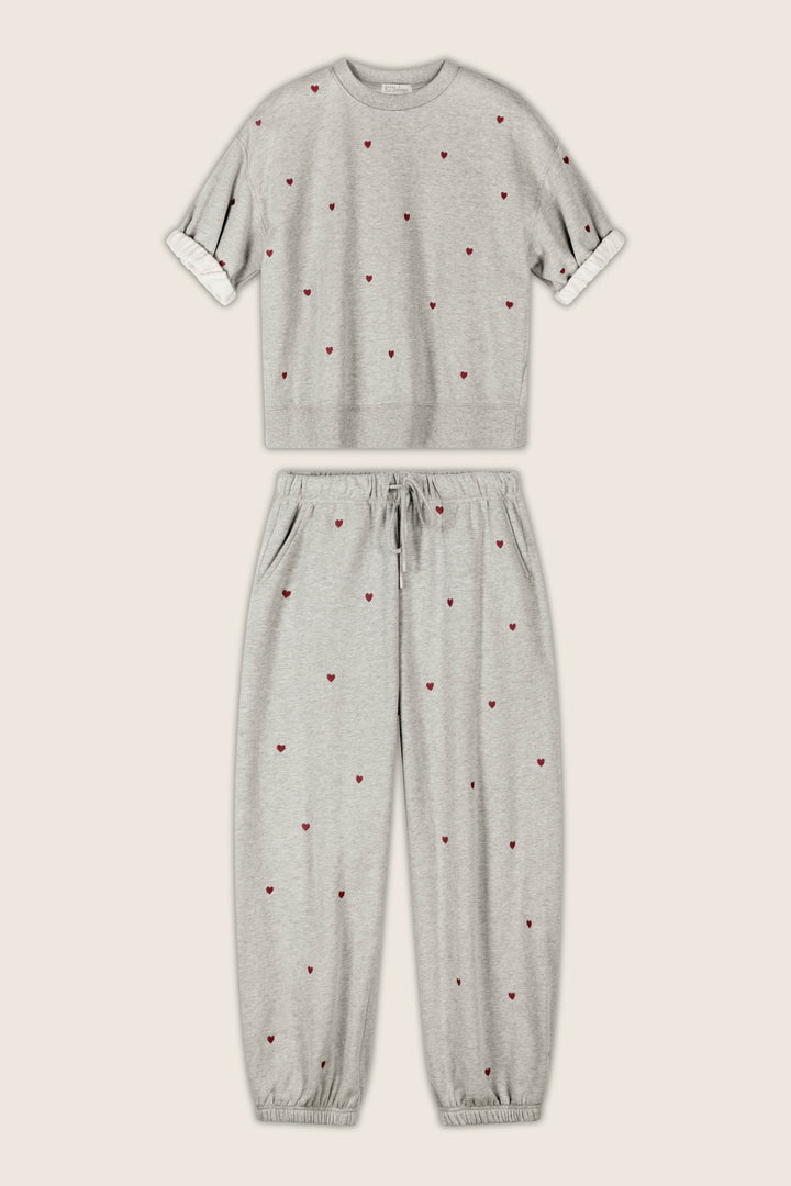 The P.J. Salvage C'est La Vie Embroidered Hearts Roll Back Short Sleeve Sweatshirt and coordinating jogger pants set, featuring small red heart embroidery, is displayed flat against a beige background. The jogger pants include a drawstring waist and elastic cuffs.