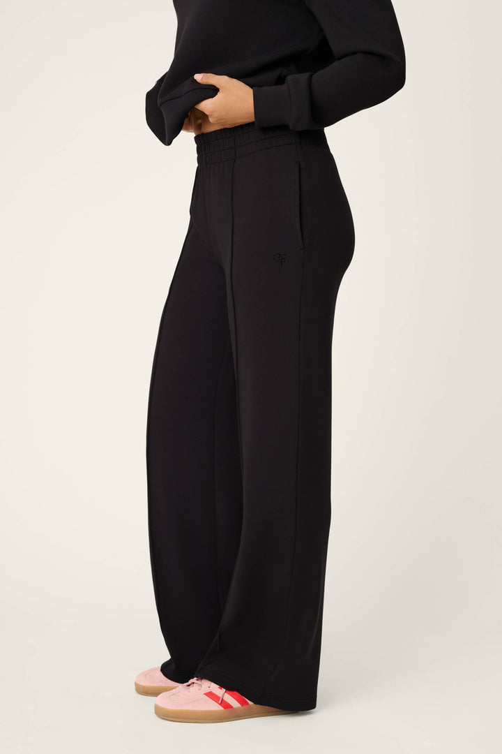 Dressed in the C'est La Vie Midnight Flights Runway Pants by P.J. Salvage, paired with a black long-sleeve top and pink sneakers with red stripes, the person stands against an off-white background with their face not visible.