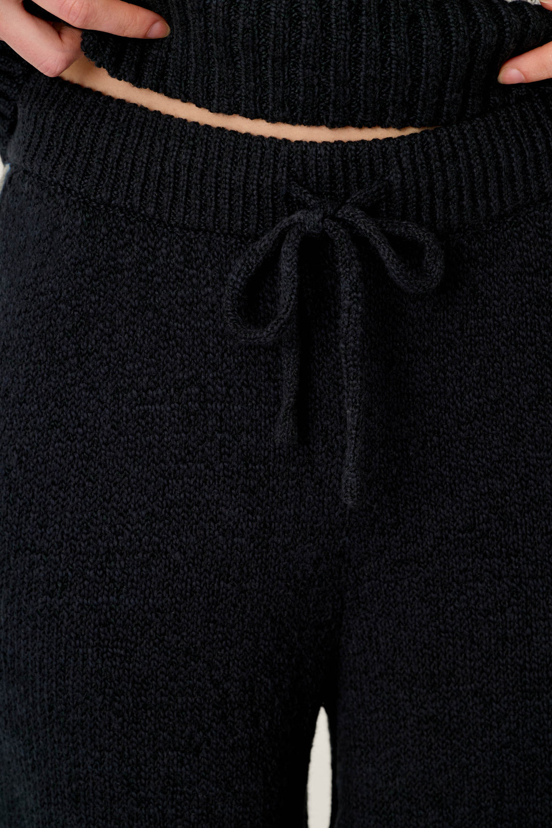 Close-up of a person wearing the C'est La Vie Suki Jogger Pants by P.J. Salvage, featuring a black textured knit fabric and a drawstring waist. The person's hands rest on their waist, with the bottom edge of a coordinating knit top also visible.