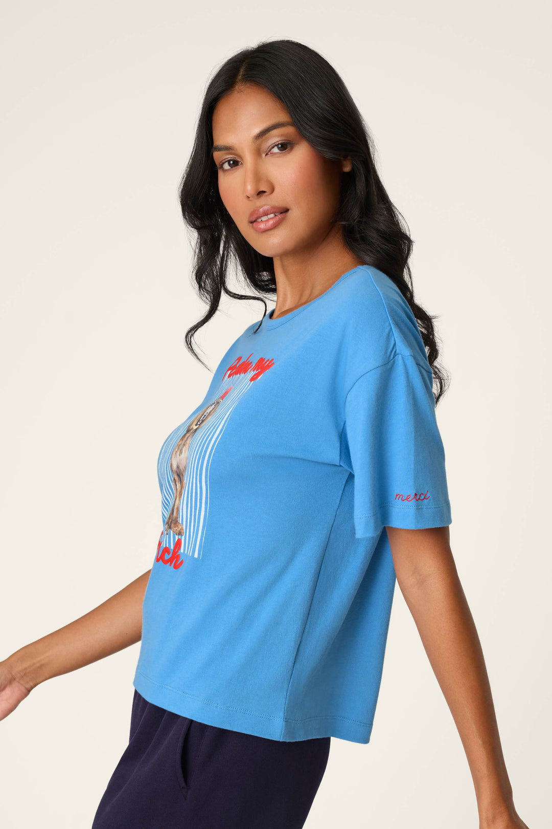 A woman with long dark hair wears the P.J. Salvage C'est La Vie "Pardon My French" Graphic T-Shirt paired with dark pants, posing against a plain light background.