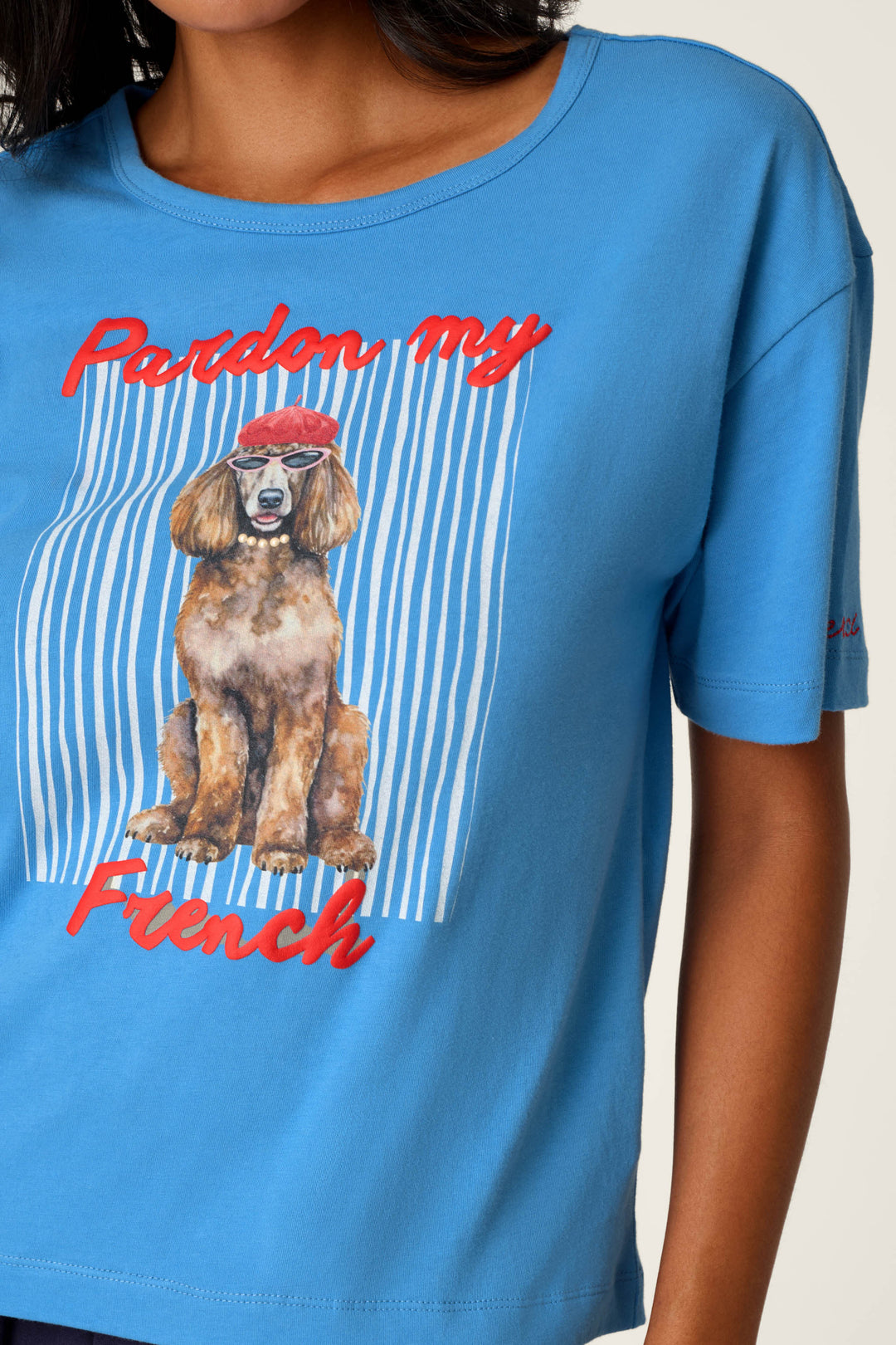 A woman wears the C'est La Vie "Pardon My French" Graphic T-Shirt by P.J. Salvage, which features a dog in a red beret and the words "Pardon my French" over a white and blue striped background.